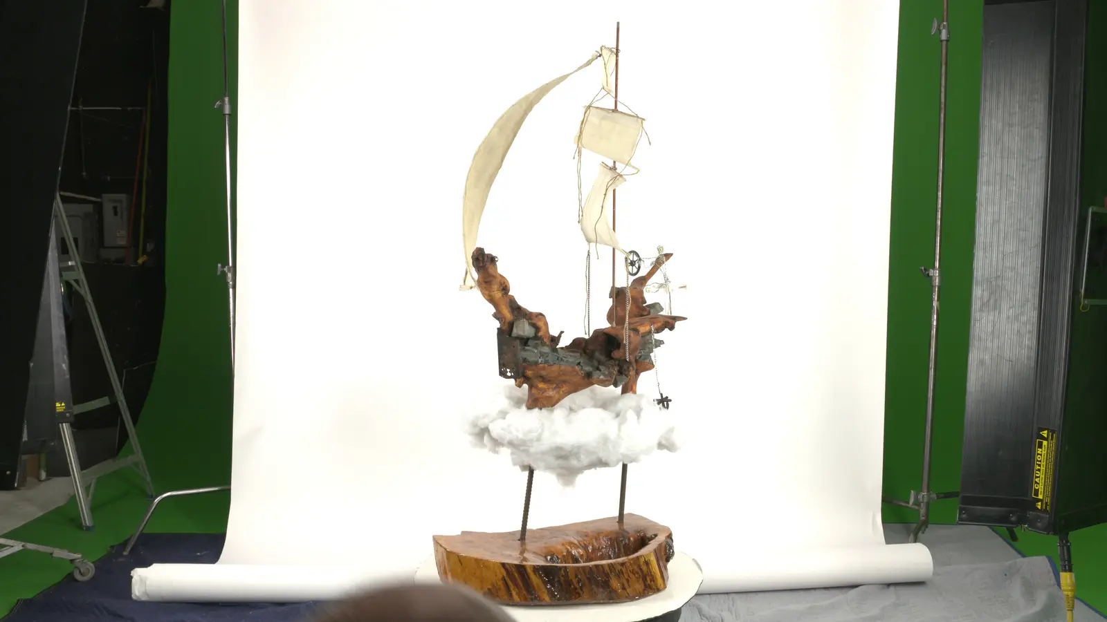 Coque en bois trouvé sculpté + voile en tissu + mât avec voilures + petits squelettes en bois sur le pont, suspendu sur nuages d'ouate, socle en rondin. — vue 5