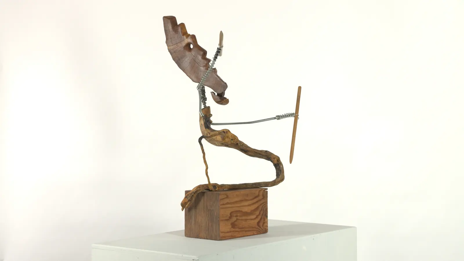 Chasseur archaïque — tête animale (cervidé / loup) en bois sculpté, cou en ressort métallique, bras tendu avec lance, corps en bois trouvé tortueux. — vue 1