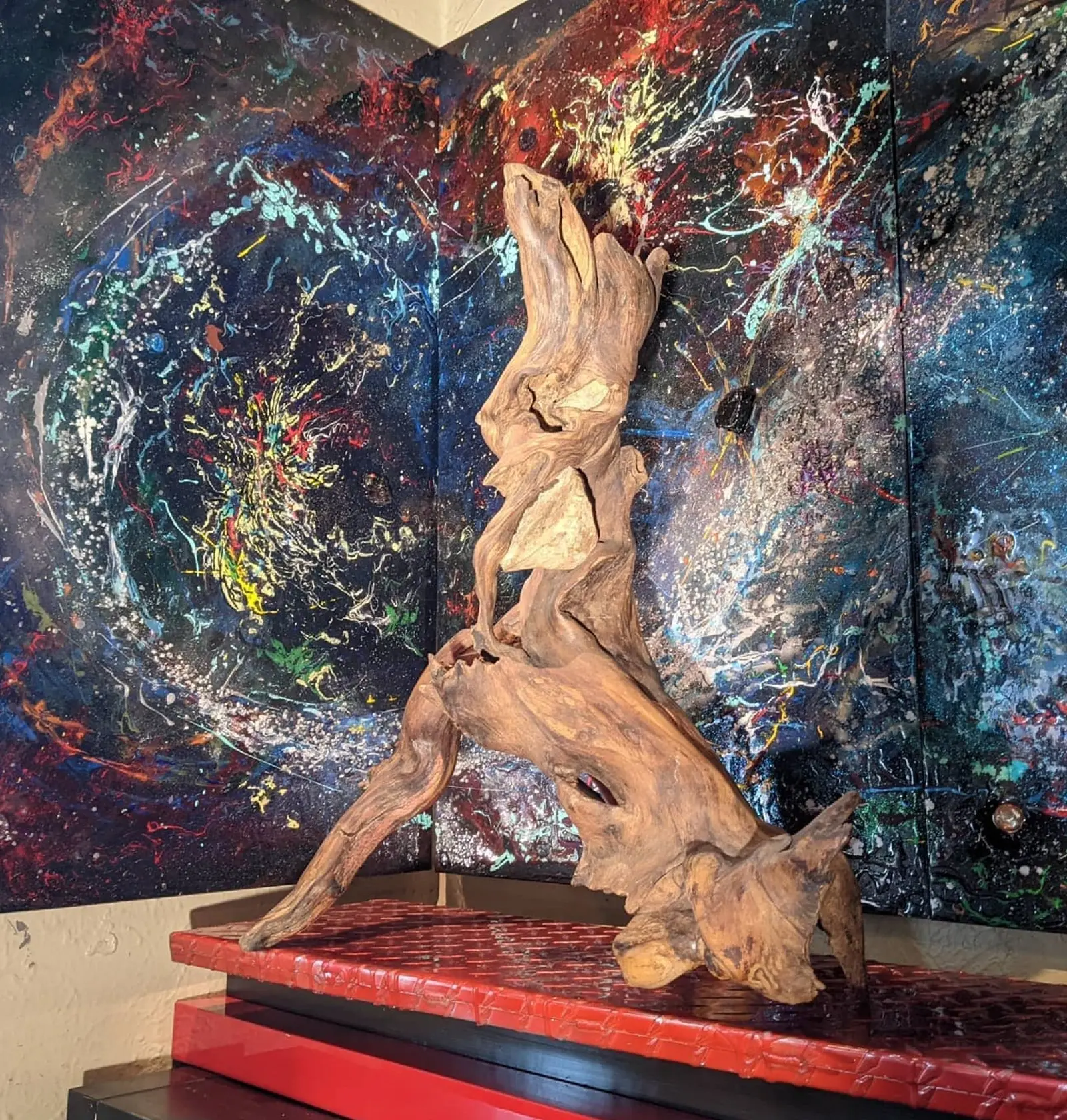 L'œuvre entière sur un plateau rouge laqué à piètement noir, dans l'angle où se rejoignent deux tableaux à projections colorées, le bois pâle et sec, deux pierres claires dans les cavités
