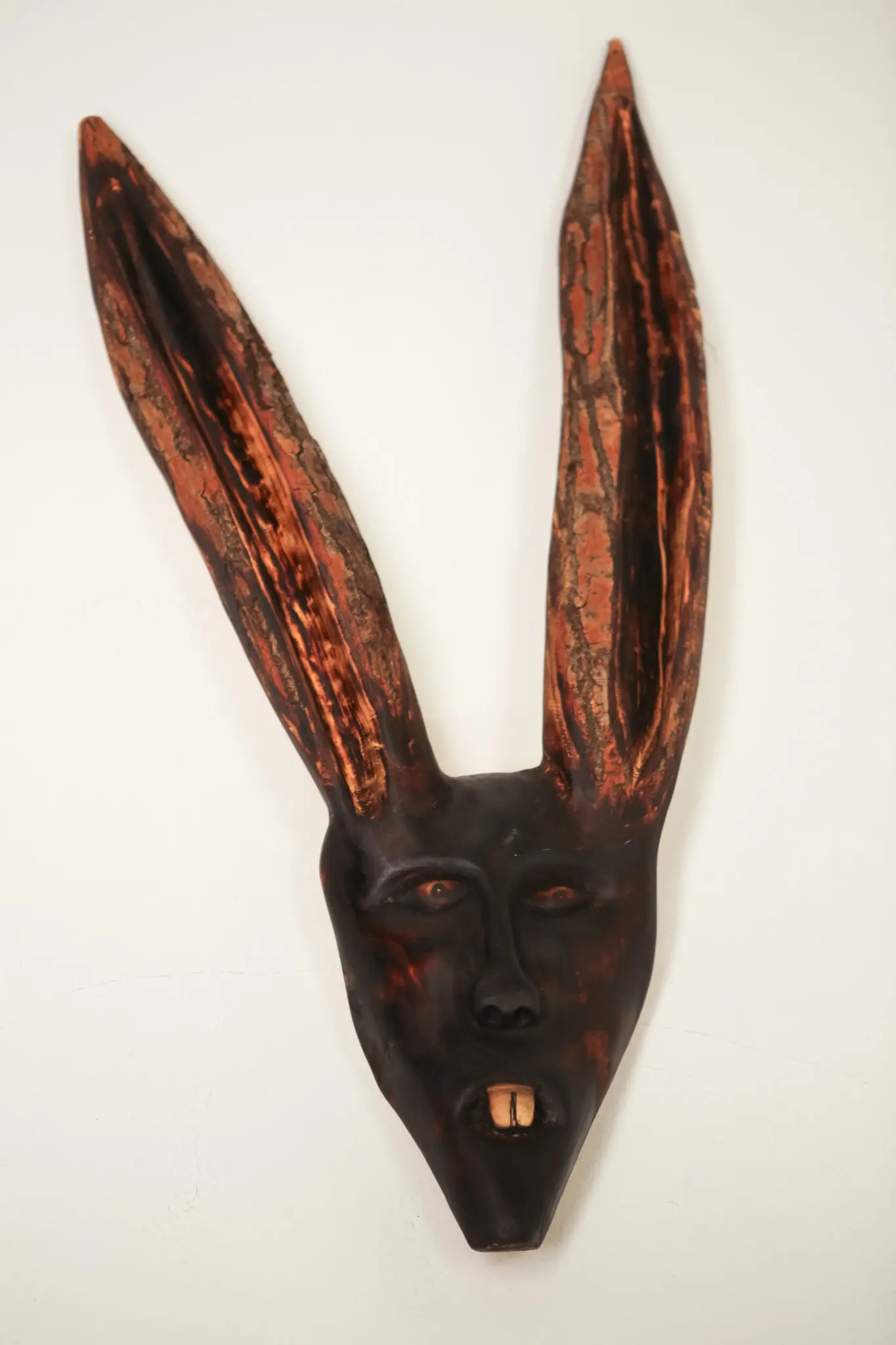 Masque léporin en bois trouvé légèrement de trois-quarts, oreilles dressées à l'écorce craquelée, yeux ambrés et patine sombre.