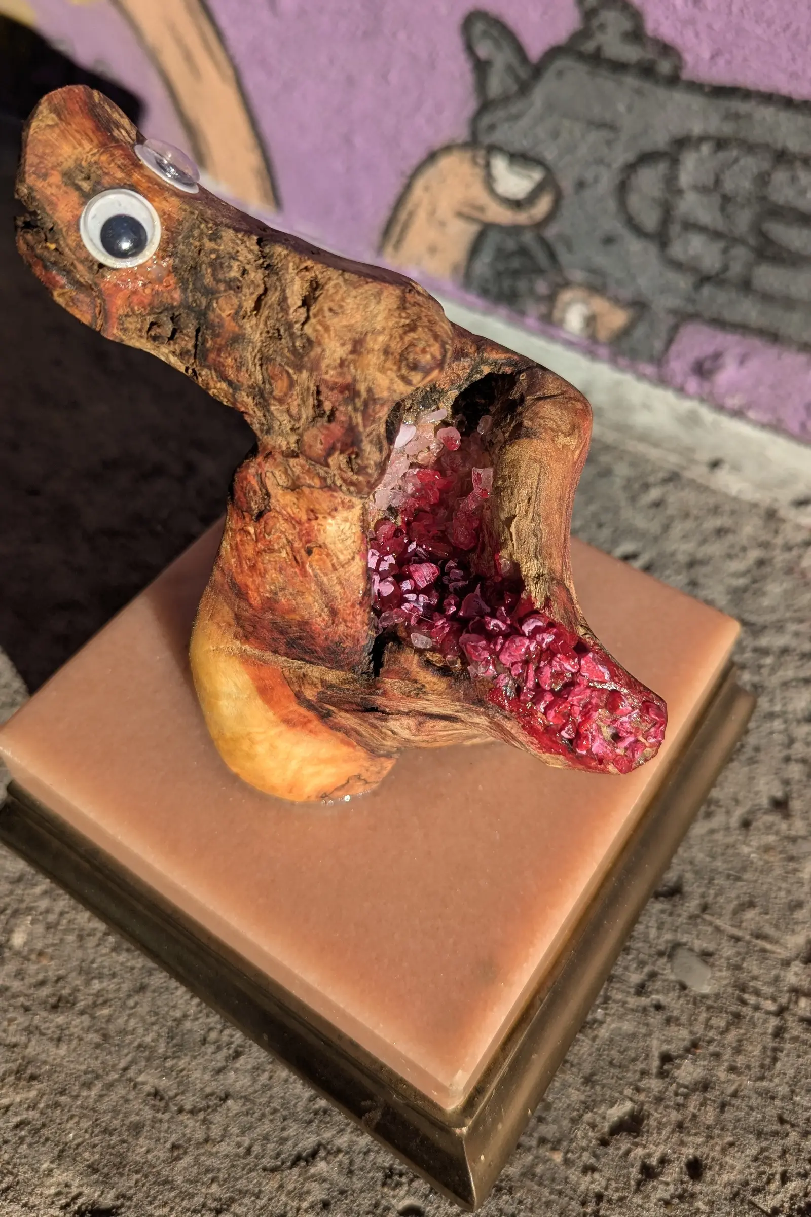 Bouche Bée vue du côté gauche, la tête allongée vers la gauche, un œil mobile de face, l'autre de biais au sommet, la cavité ouverte vers la droite, fragments rouges plus denses à la pointe, lobe de bois blond au pied, socle de marbre rose