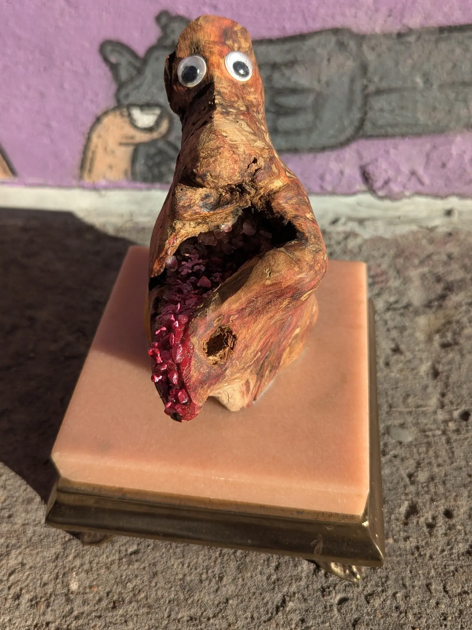 Bouche Bée de face, tête dressée, deux yeux mobiles vers l'objectif, la cavité ouverte à gauche du rose pâle au rouge, le petit trou rond au flanc droit, socle de marbre rose à rebord doré, mur violet à figure peinte en gris