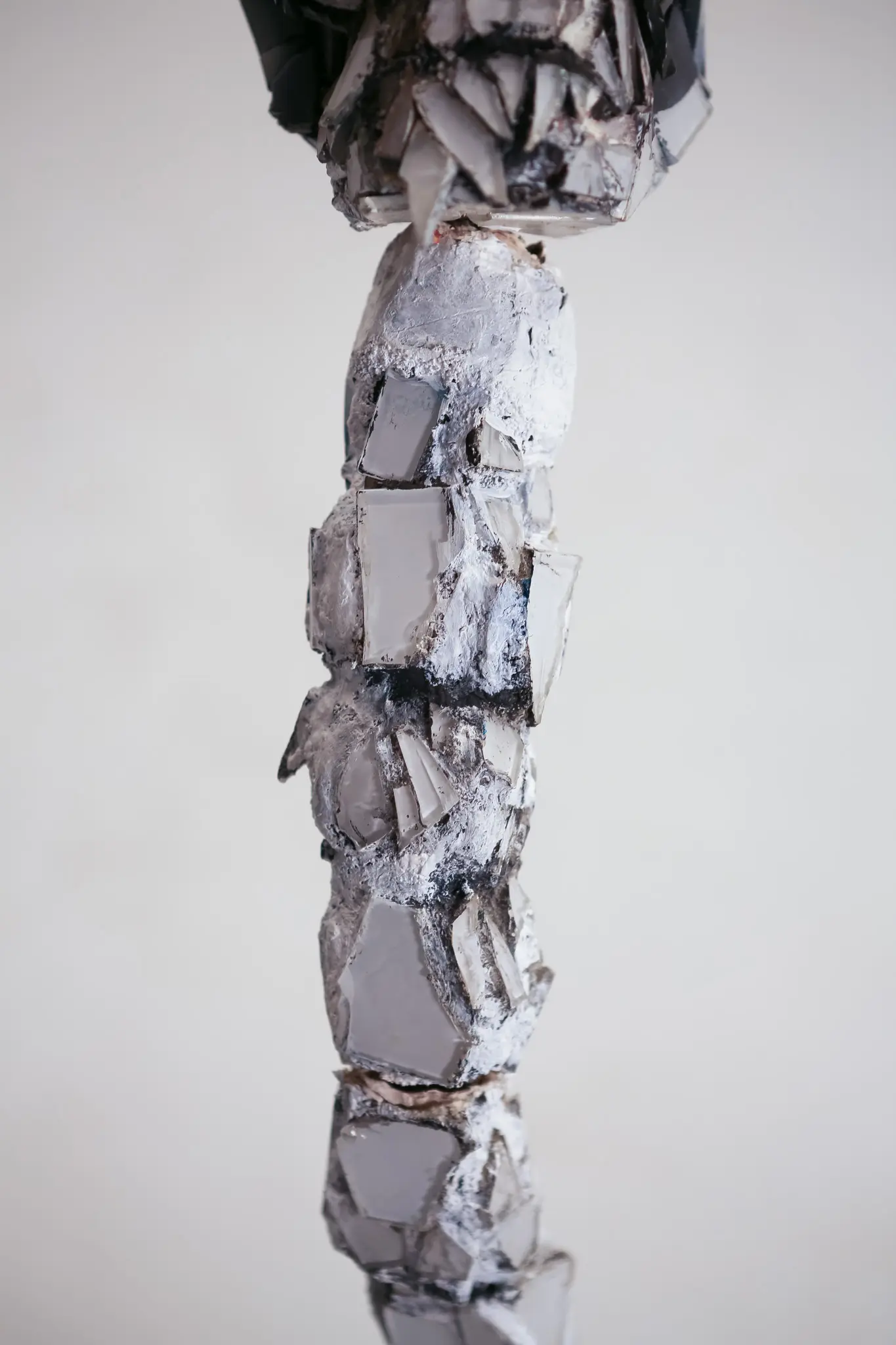 Detail de la colonne vertebrale segmentee, plaques de miroir et de verre serties dans un mortier pale et craquele formant des vertebres empilees.