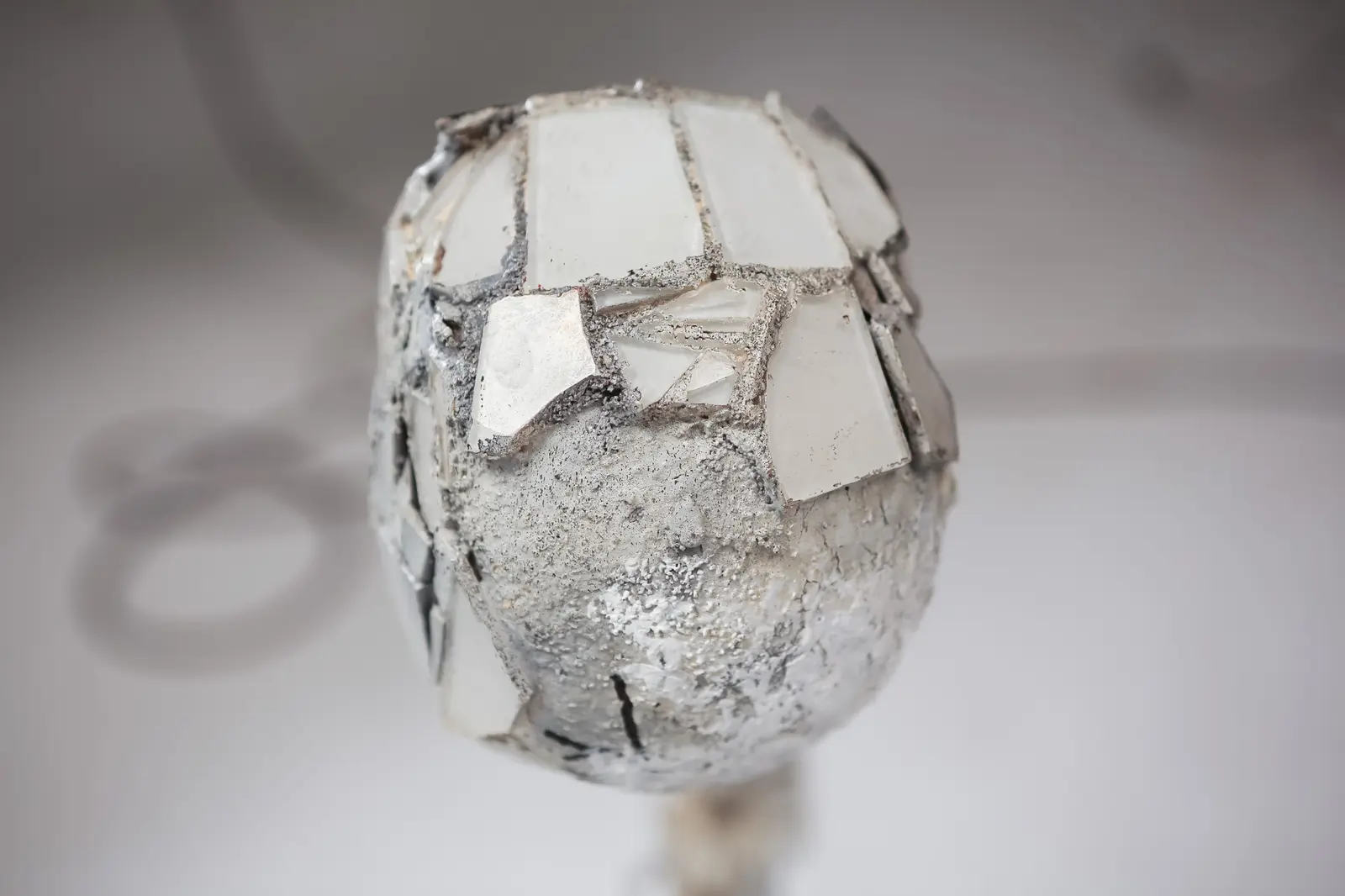 Vue rapprochee du sommet du crane, calotte en mortier gris clair partiellement couverte de tessons de miroir et de carreaux de verre tessellated.