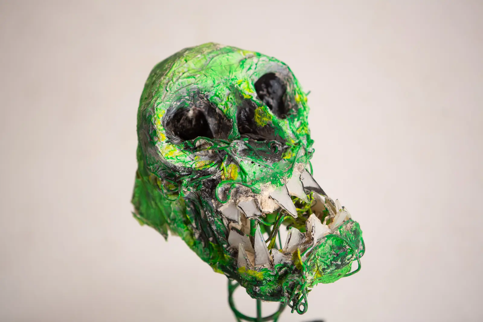 Crâne sculpté en papier peint en vert vif, orbites noires creuses et dents faites d'éclats de verre, vu de trois-quarts.
