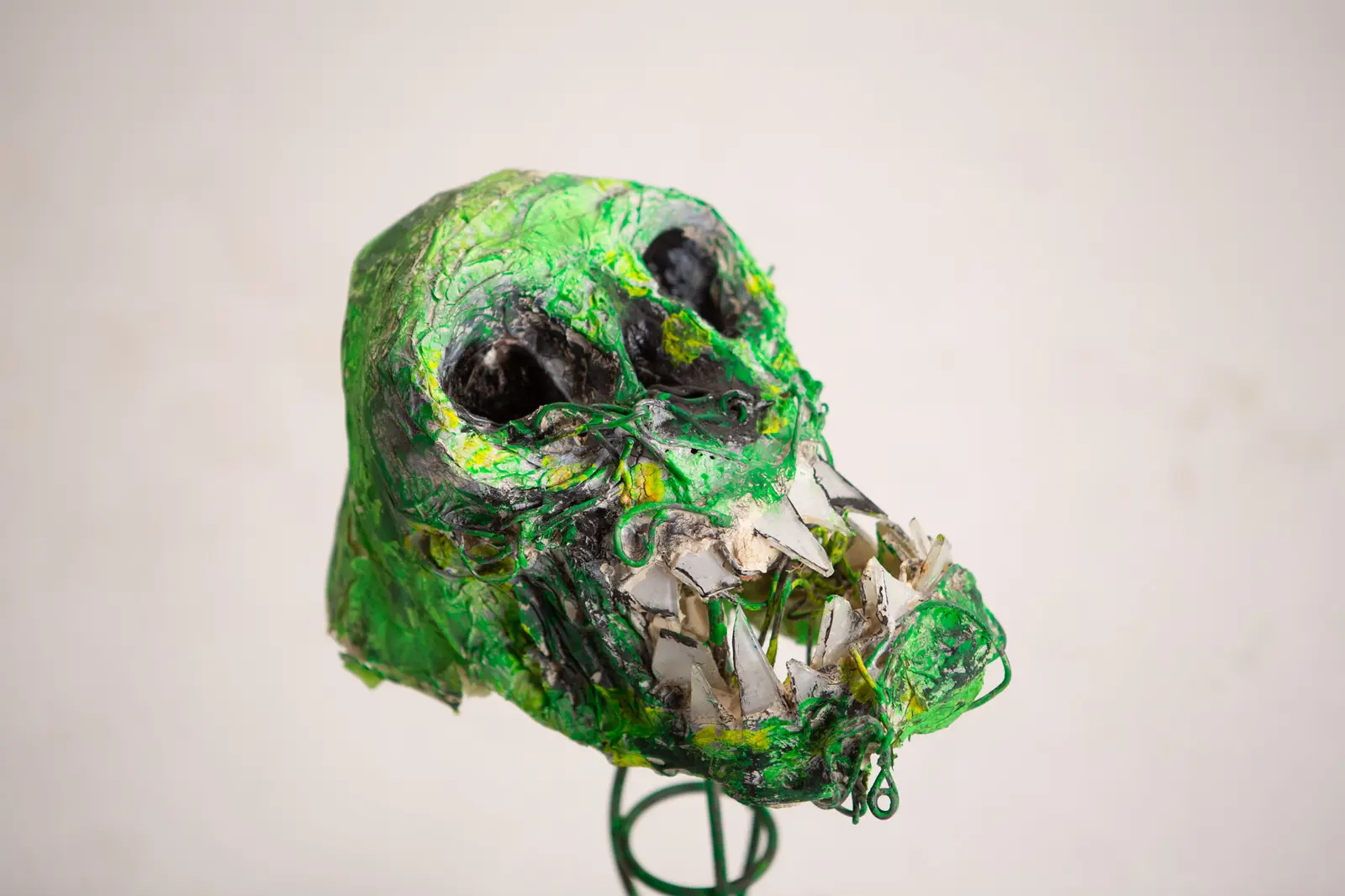 Profil de la figure crânienne verte, fil de fer enroulé autour du museau et mâchoire garnie d'éclats de miroir.