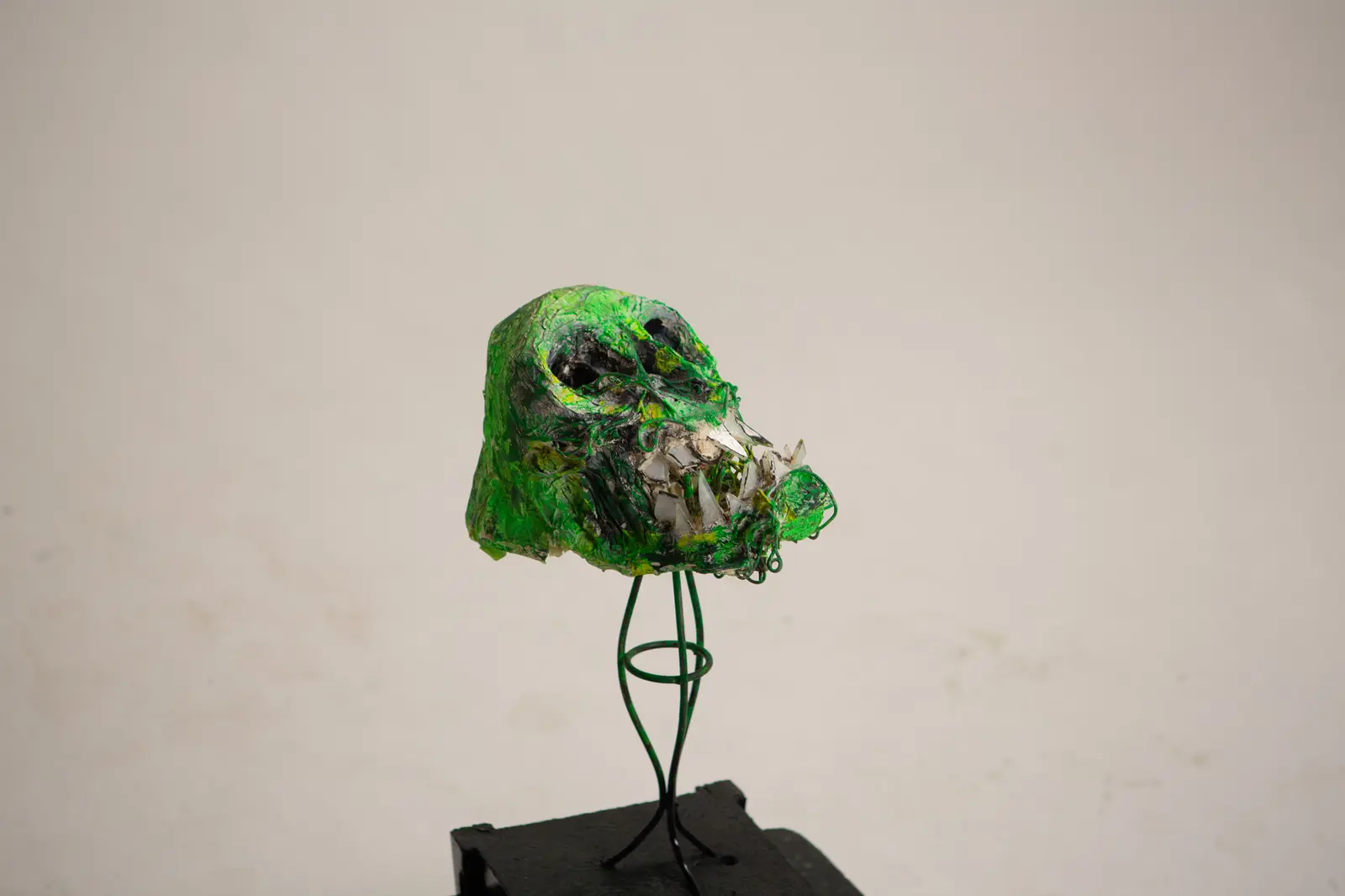 Vue d'ensemble de la sculpture verte montée sur tige de fil de fer torsadée au-dessus d'un socle sombre.