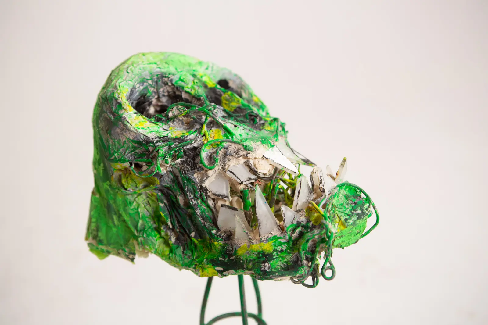 Détail du museau allongé de la figure verte, dents d'éclats de verre et de miroir saillantes, fil de fer apparent.
