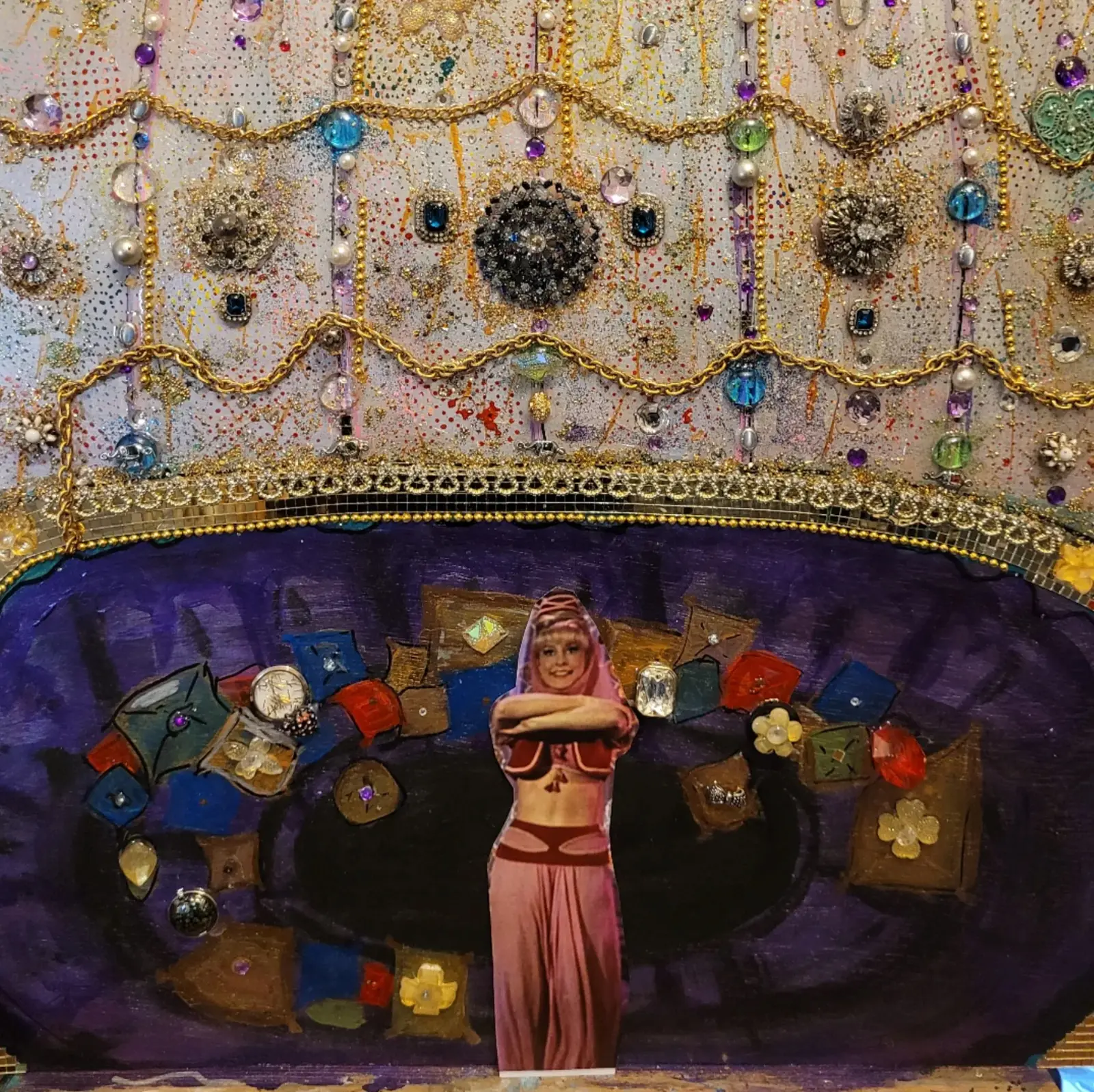Assemblage mural : panneau clair couvert de broches, de perles et de chaînes dorées en festons, éclaboussé de rouge et de jaune, surmontant une alcôve violette où une figure découpée dans une photo, en costume rose, se tient parmi des coussins peints, œuvre de Robert Bibeau