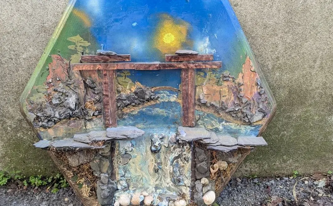 Gros plan du diorama : le pont et son arche au-dessus du ruisseau, détail des berges de pierres et du soleil peint