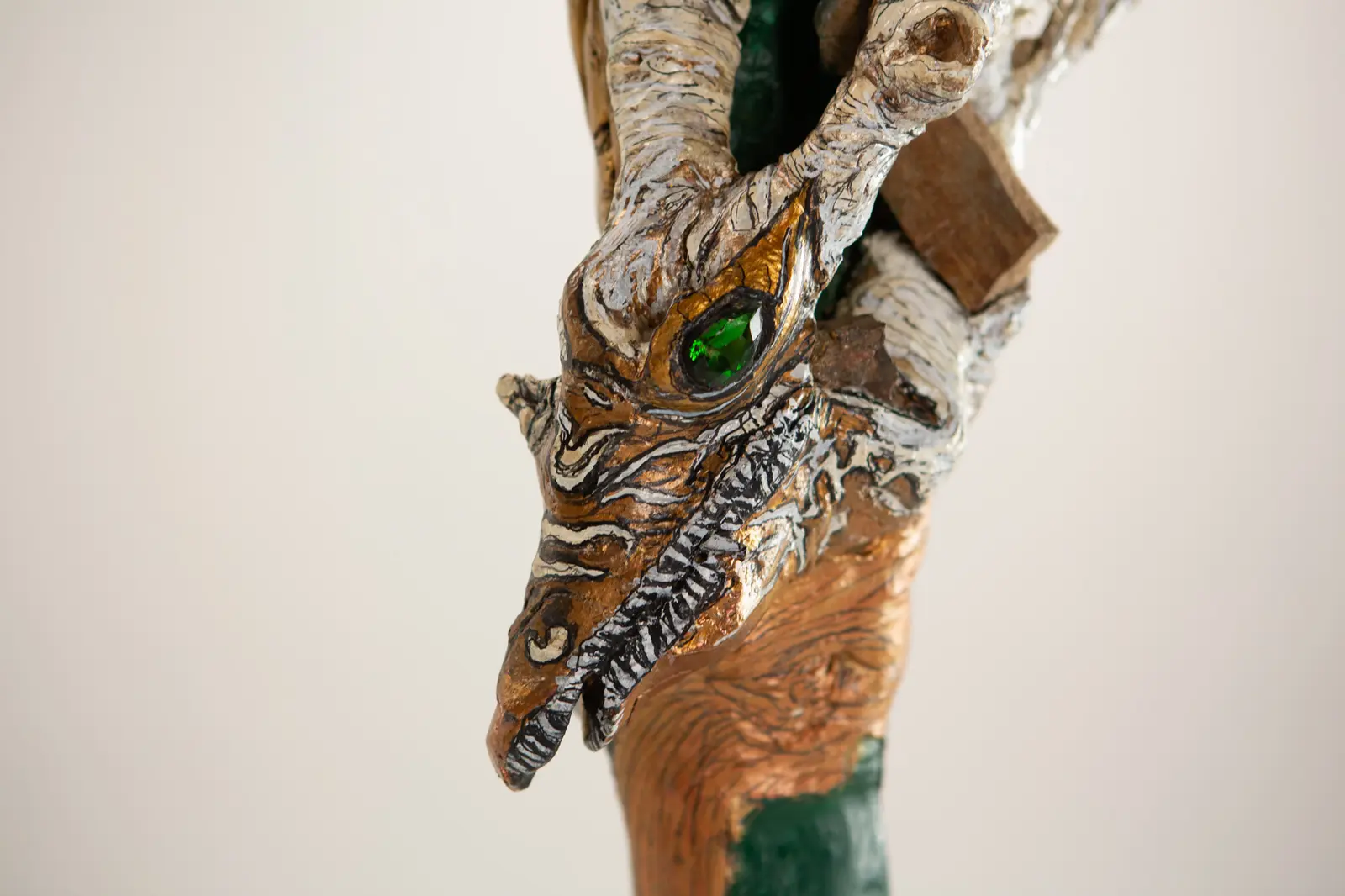 Detail rapproche de la tete reptilienne, oeil de verre vert facette, museau strie noir et blanc, dorure et bois sculpte.
