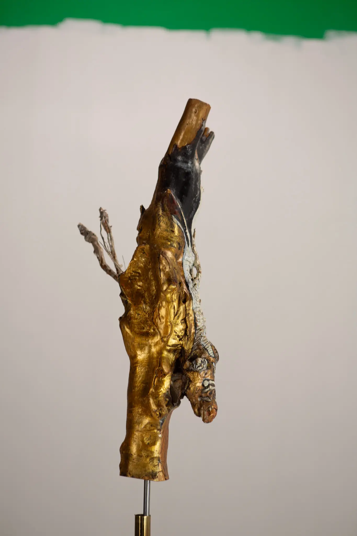 Forme verticale en bois sculpte, surface doree et sommet noirci, montee sur tige metallique et socle de metal.