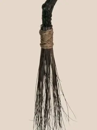 Tête du balai sculpté : ligature de corde et fagot de brindilles retombant, bois noueux peint en noir, sur fond clair.