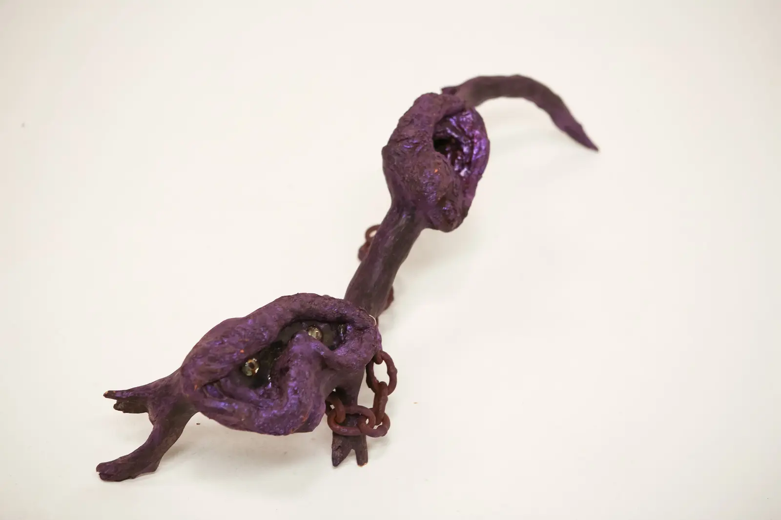 Sculpture vue en contre-plongée, tête aux yeux de verre au premier plan, corps en branche violet redressé vers la cavité arrière et la queue effilée.