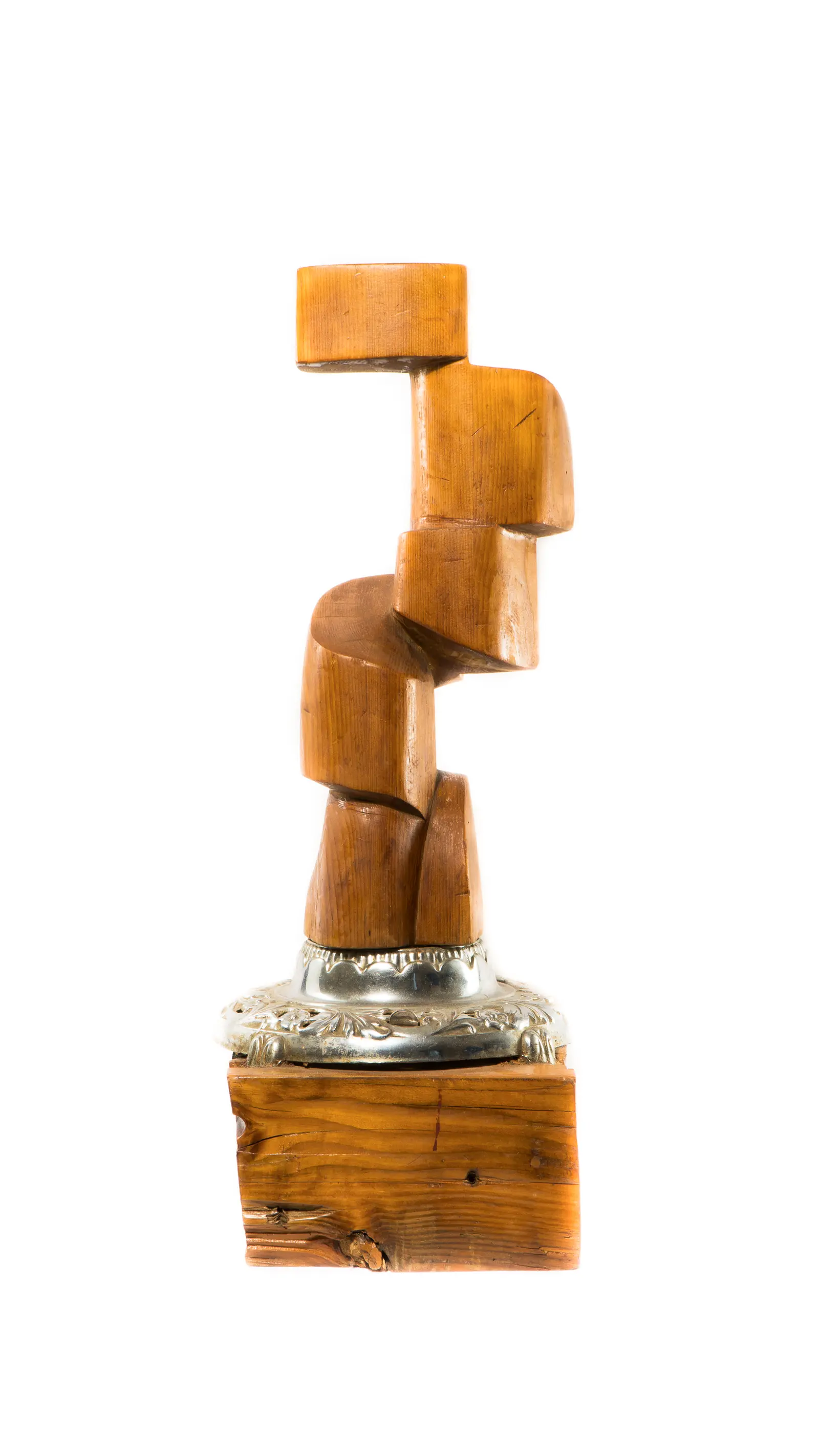 Le boss : colonne de blocs de bois empilés en zigzag sur une base argentée ornée posée sur un bloc de bois brut, vue frontale en studio, œuvre de Robert Bibeau