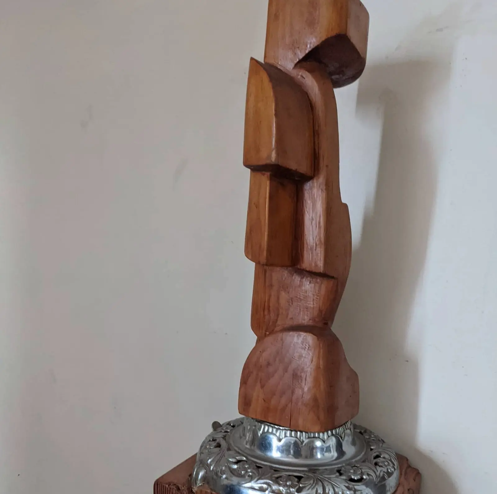 Close view of the stacked pale wood blocks against a plain white interior wall, the top of the stack running past the edge of the frame, the round chased silver base showing along the bottom