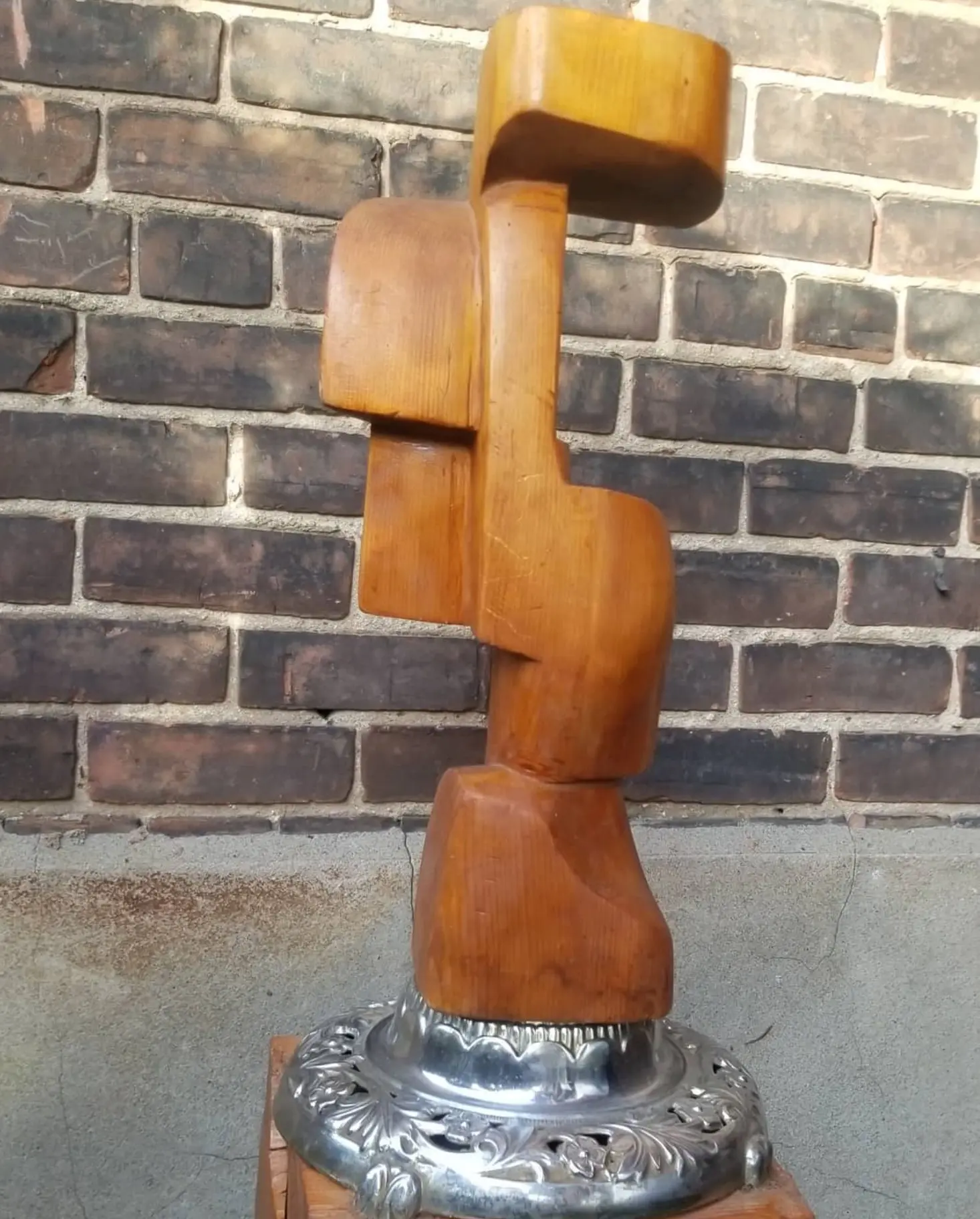 The whole piece photographed outdoors in bright sunlight in front of a brown brick wall, standing on its round chased silver base, which rests on a wooden block