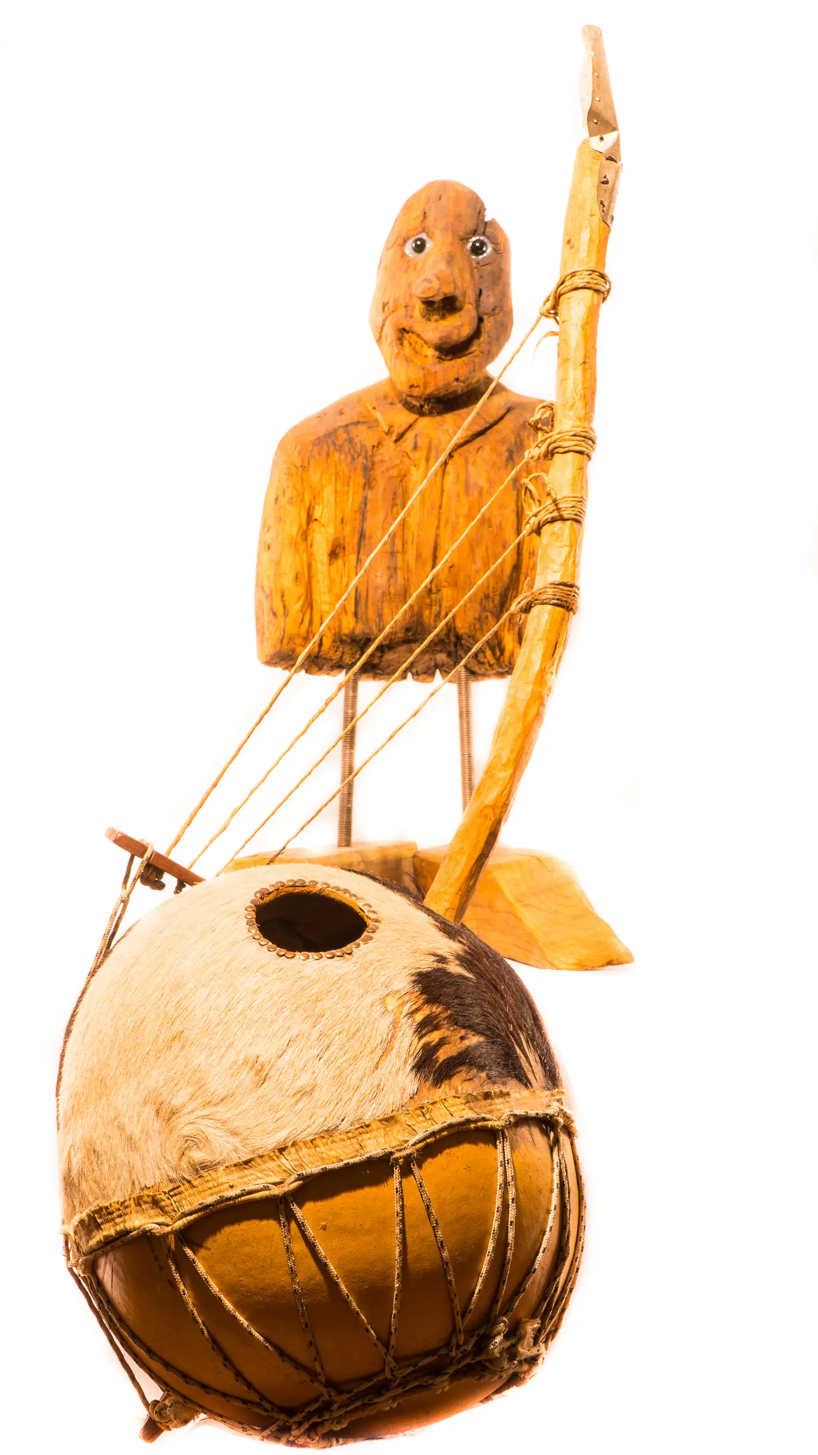 Sculpture : buste de bois souriant aux yeux mobiles derrière un instrument à cordes en calebasse tendue de peau, œuvre de Robert Bibeau