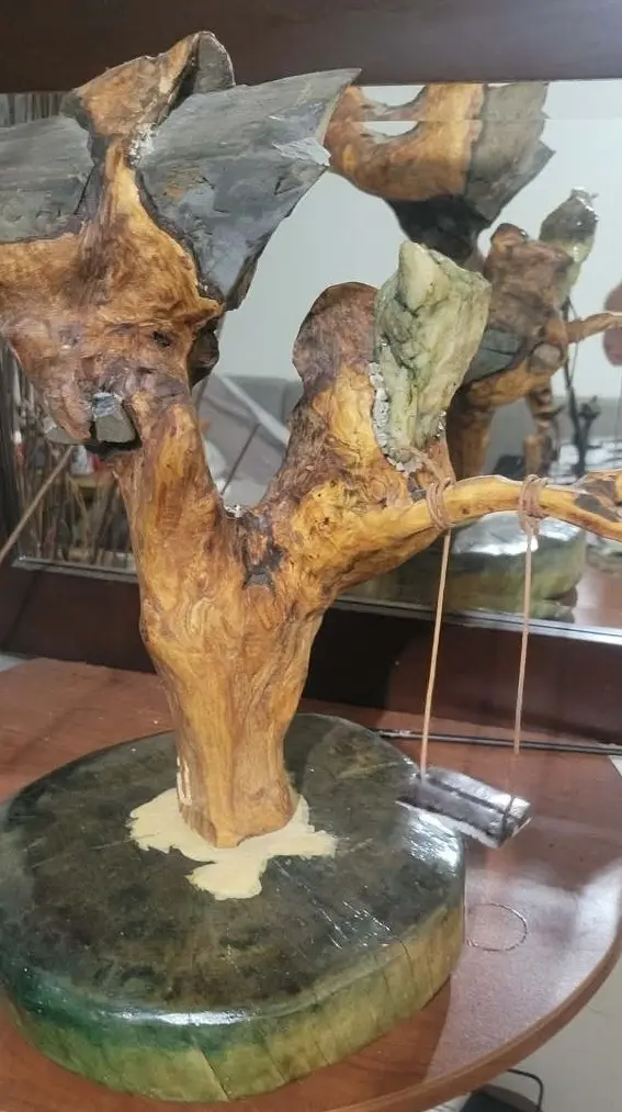 La balançoire magique vue de face sur une table, sculpture en bois trouvé surmontée de pierres et d'un cristal, avec sa balançoire suspendue.