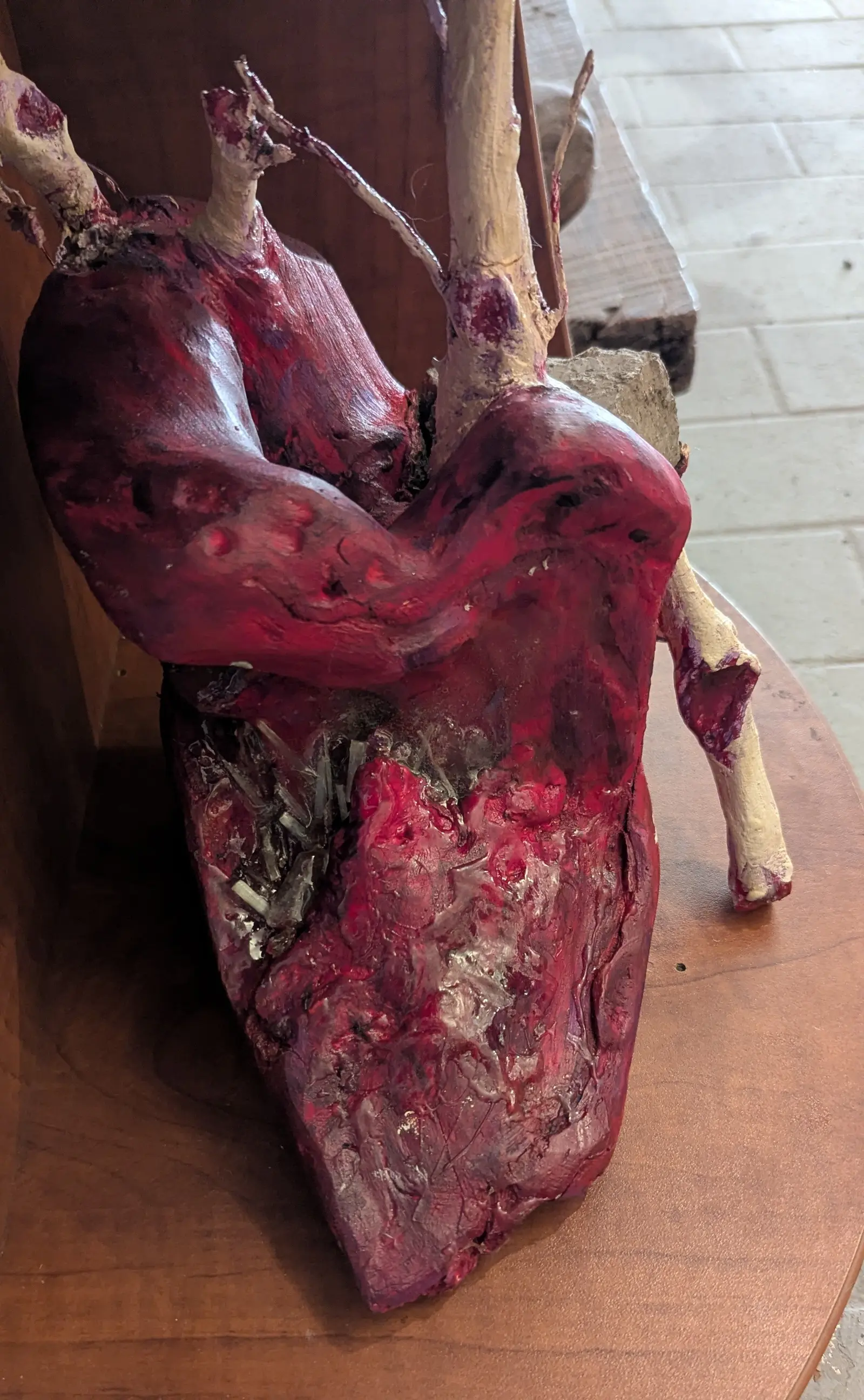 I Give You My Heart, set on a wooden shelf with no base: wooden heart painted a deep glossy red, pale vessels rising from the top, one pale branch curving down to the shelf, mirror shards in the lower part