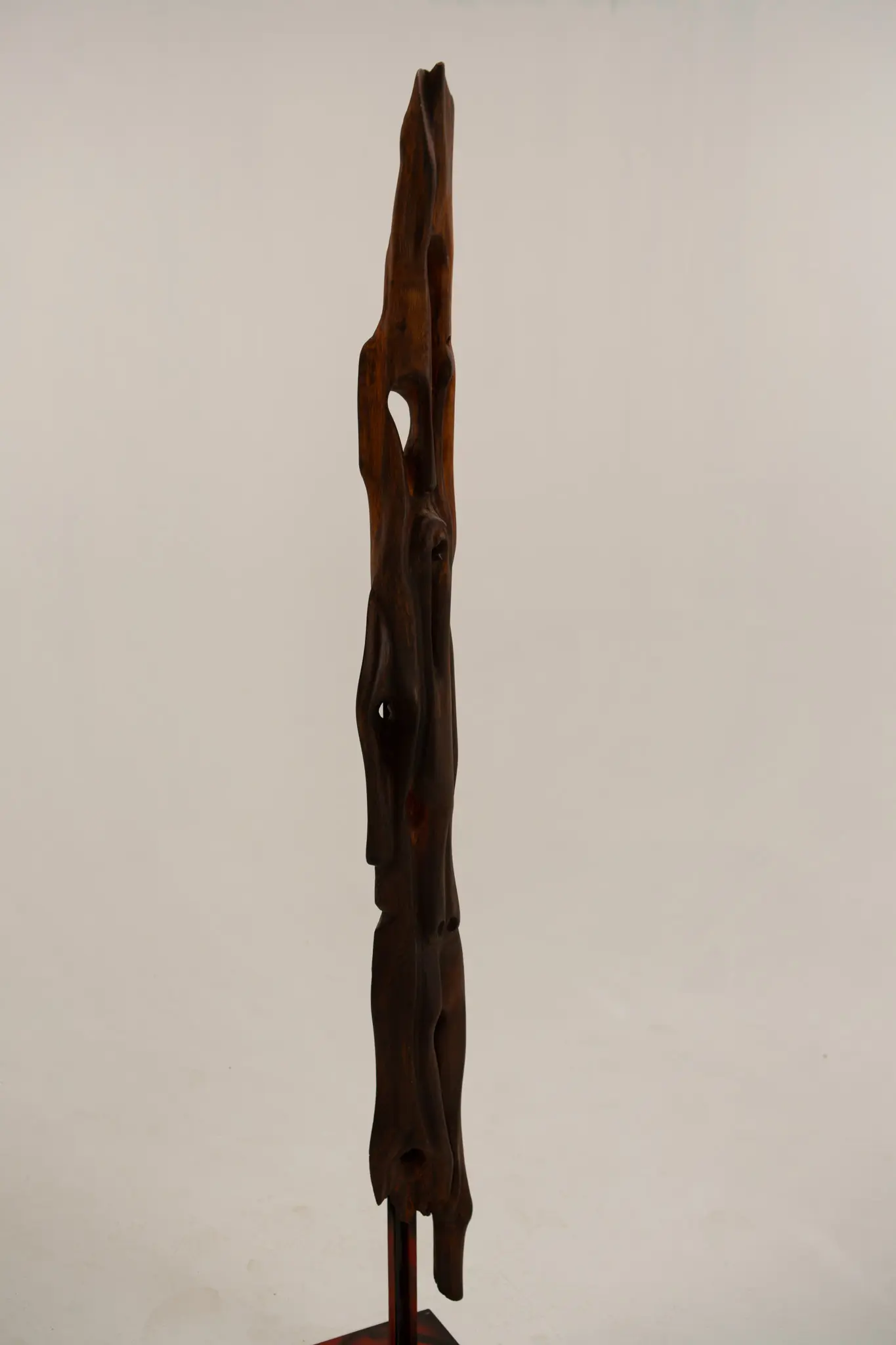 Vue de profil de la figure dressée en bois sculpté, silhouette étroite et sinueuse révélant le fil du bois et de petites ouvertures.