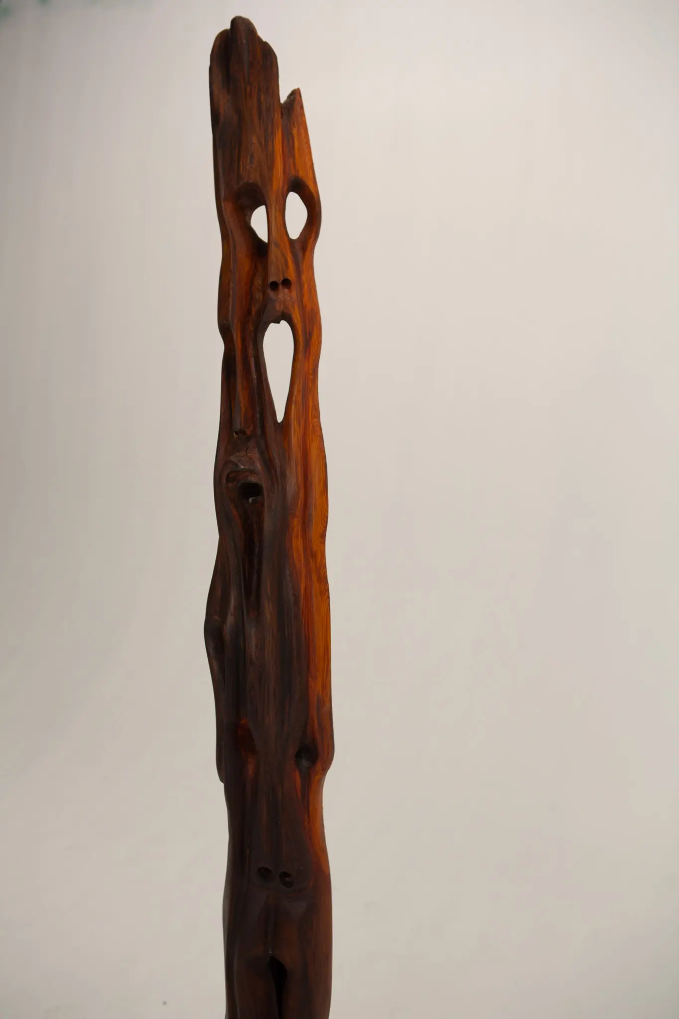 Détail de la partie haute de la sculpture en bois, cavités oblongues percées et trous oculaires alignés sur le fil ondoyant du bois verni.