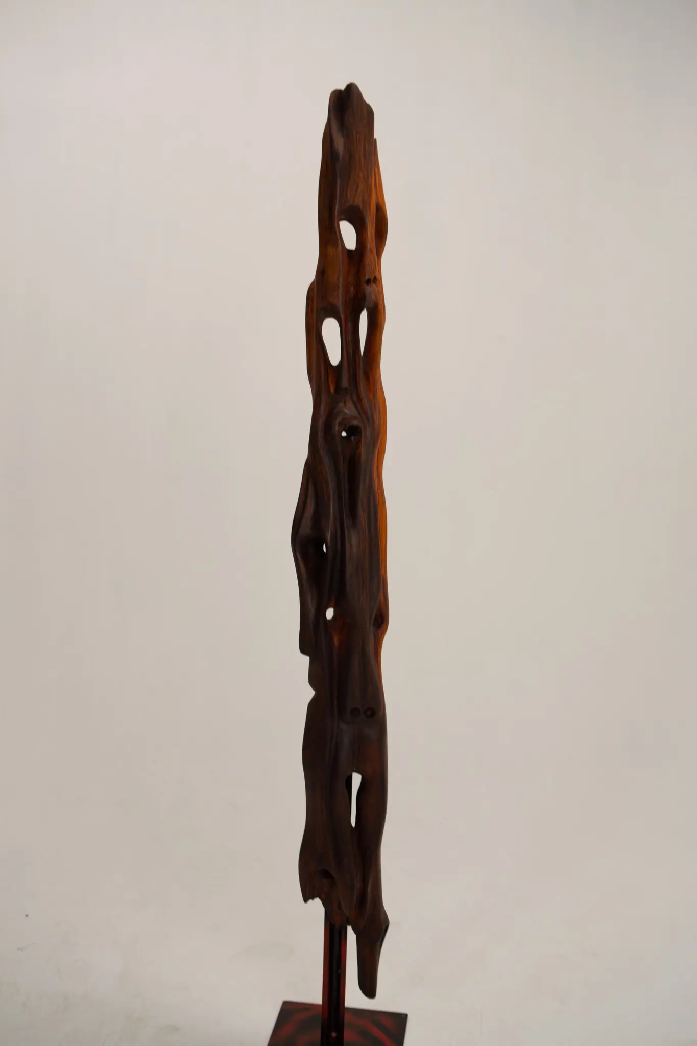 Vue d'ensemble de la figure dressée en bois trouvé sur sa tige métallique, succession de cavités creusées de haut en bas.